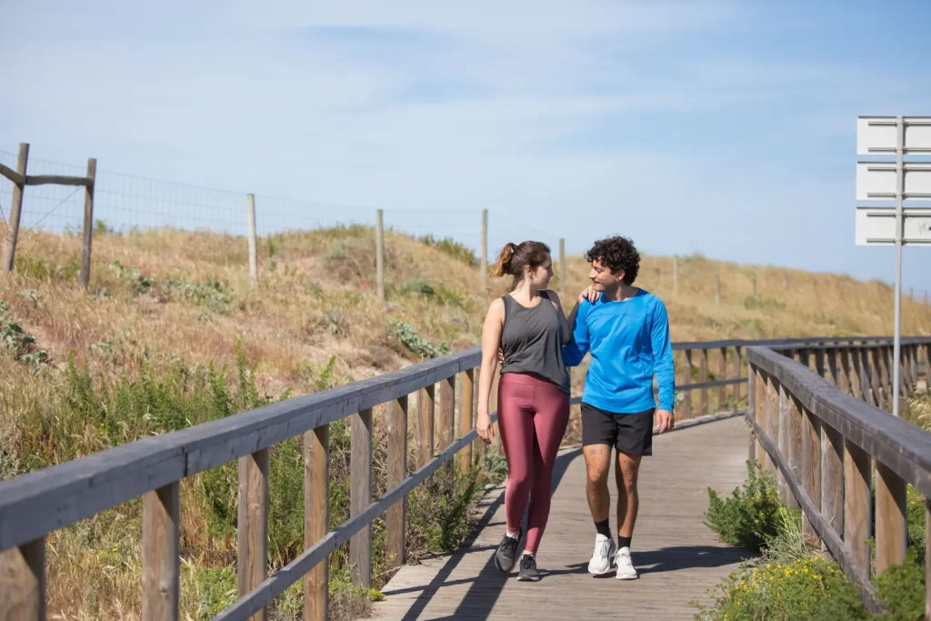 Two people walking and talking on a wooden boardwalk on a sunny day