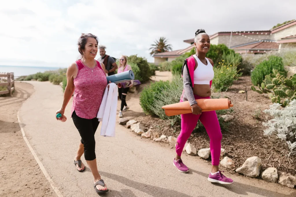 Two women walking outdoors carrying exercise mats