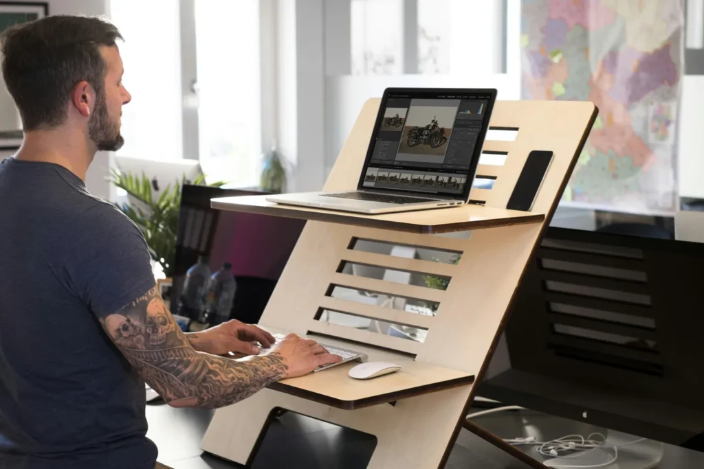 Man typing on a laptop set on a wooden standing-desk converter
