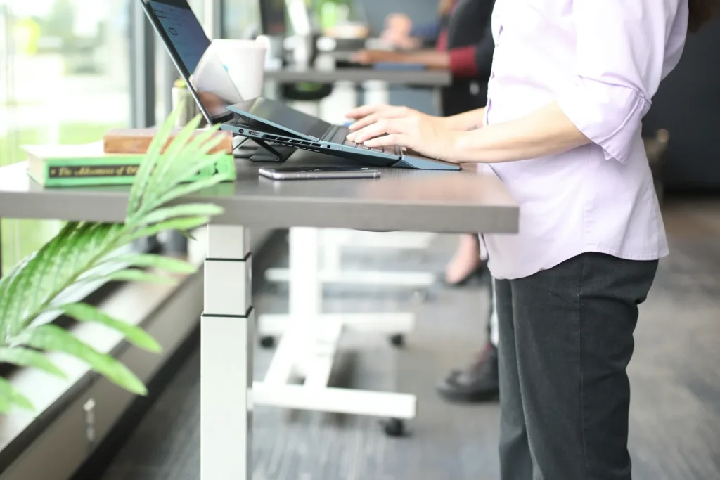 Woman working on a laptop at a standing desk in a bright office