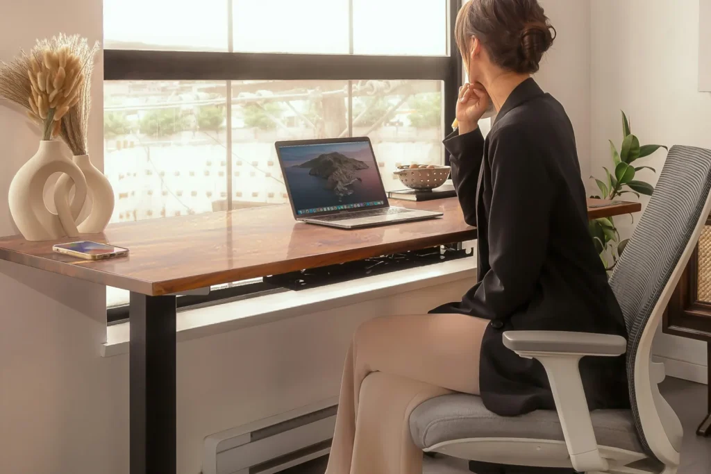 Woman in an office chair beside a desk with a laptop, looking out a window