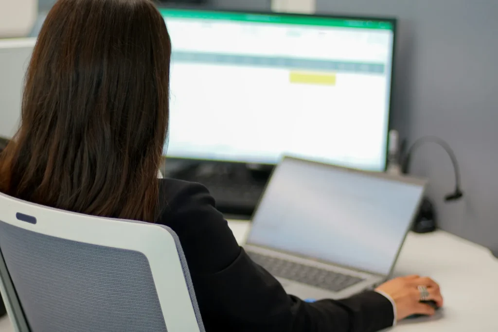 Woman using a laptop connected to a monitor showing a spreadsheet